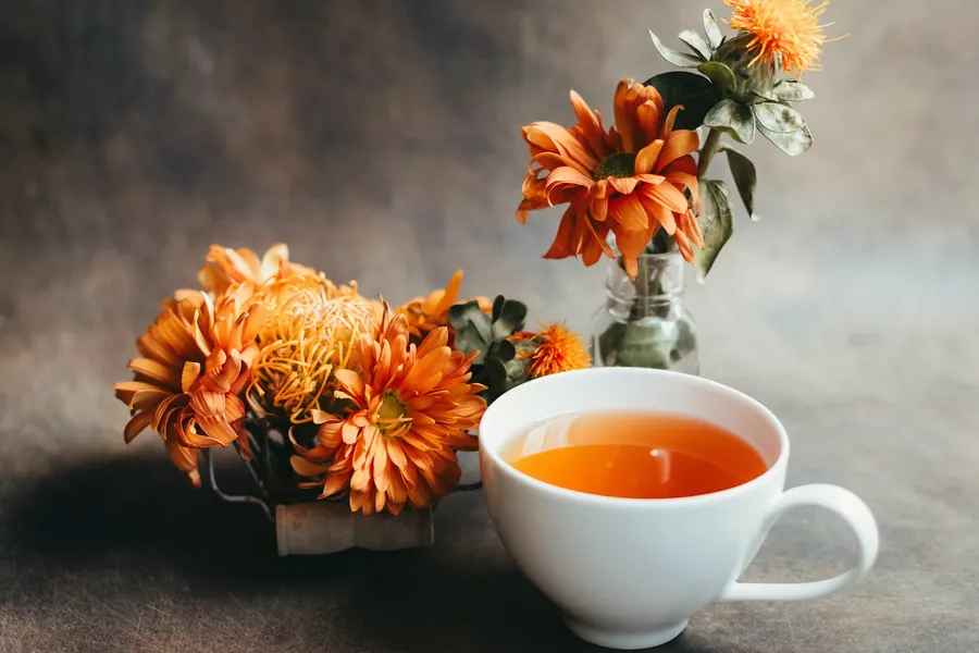 Tasse de tisane posée près d'un vase de soucis orangés